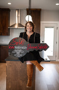 Wood Realtor key with Woman sitting on a wooden platform with a 'Sold!' sign in a kitchen setting