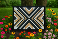 Geometric patterned wall art framed in black, surrounded by colorful flowers outdoors.